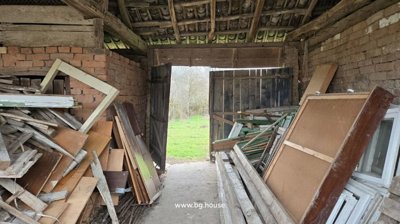 Interior view of a barn or storage room showing wooden beams and stacked wood, frames, and other materials.