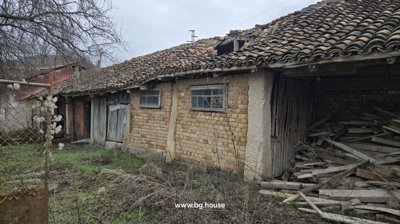 Exterior of brick outbuildings with tiled roof and wooden doors surrounded by grass and weeds.
