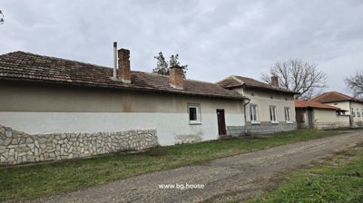Side facade of a Bulgarian house showing multiple chimneys, windows, and a dirt road alongside the building.