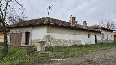 Corner of a Bulgarian house with stone fence, leafless tree, and tiled roof under cloudy sky.