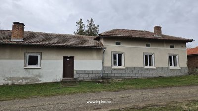 Front facade of a Bulgarian house featuring several windows and a brown door, with grass in the foreground.