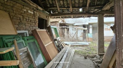 Covered outdoor storage area containing wooden window frames and other materials, with buildings visible beyond.