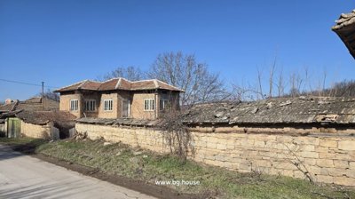 Stone wall with tiled roof along a village street near a two-storey brick house