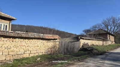 Stone wall and green wooden gate with brick house and tiled roofs behind