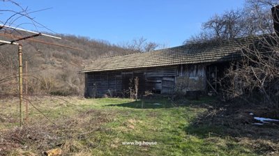 Wooden barn with slatted walls and tiled roof adjacent to a brick house