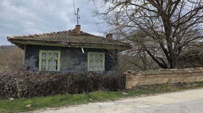 View of a traditional house with green window frames and a tiled roof next to a paved road under a cloudy sky.