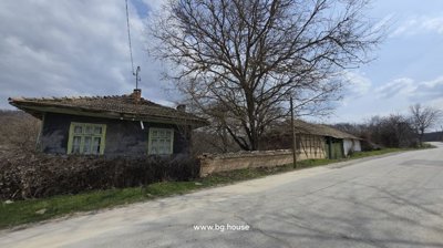 Wide view of a traditional house and adjacent outbuildings along a rural road with leafless trees.