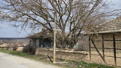 Rural house partially visible behind a brick wall with leafless trees and a distant view of the village landscape.