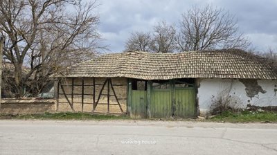 Weathered brick and wood outbuilding with green doors located along a quiet village street.