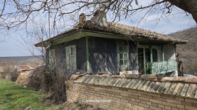 Close-up view of an old rural house featuring green window frames and a wooden balcony behind a brick wall.