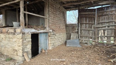Exterior of a stone and brick outbuilding featuring open wooden doors and a dirt floor covered with wood chips.
