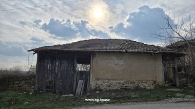 View of an old wooden barn with a tiled roof and plastered walls, set against a partly cloudy sky.