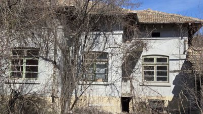 Exterior view of an old house showing three windows and leafless trees in front during winter