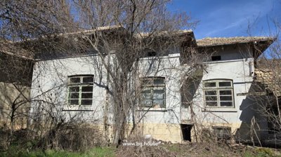 Exterior view of an old house showing three windows and leafless trees in front during winter