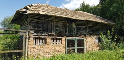 Barn with brick lower walls and wooden upper walls, topped with a tiled roof, surrounded by vegetation.