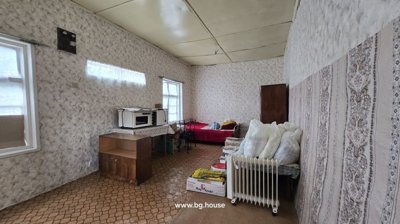 Interior of a room showing wallpapered walls, a bed covered with blankets, a wooden wardrobe, a microwave on a table, and a portable heater