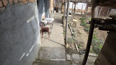 Concrete walkway alongside a brick and plaster wall with a table and chair, overlooking a garden area.