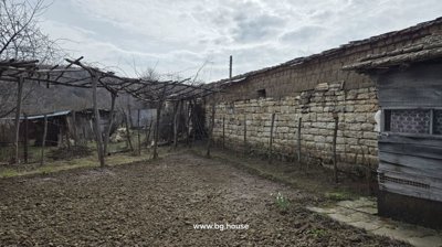 Garden area featuring tilled soil, wooden trellis overhead, stone wall, and fenced yard.