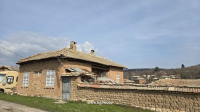 Brick house behind a stone garden wall with tiled roof, set against a backdrop of rural village houses and hills