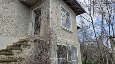 Corner view of the two-storey house showing external stairs, windows, and leafless trees around.