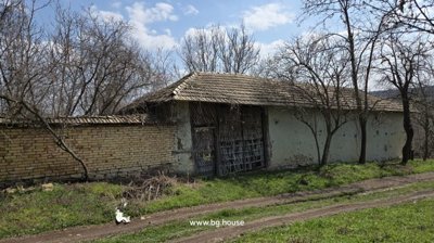 Brick fence with a large wooden gate and a tiled roof structure behind, surrounded by leafless trees.