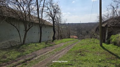 Dirt road running alongside a brick fence and leafless trees, with a view of the distant landscape.
