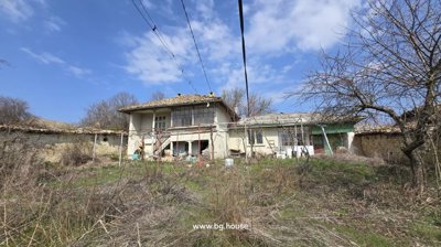 View of a two-storey Bulgarian house with external stairs and a garden with dry grass and vines in Palamartsa village