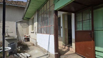 Side entrance of the house with a brown door, window, small tiled porch, and outdoor sink surrounded by various items