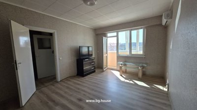 Bright living room featuring light wood flooring, patterned wallpaper, a TV on a black chest of drawers, and an open door leading to the balcony.