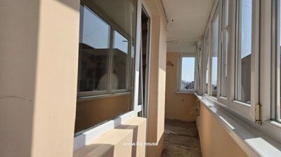 Long enclosed balcony with beige walls and white framed windows allowing natural light
