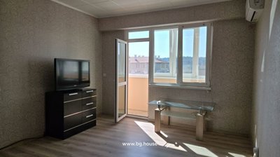 Spacious living room showing a TV on a black chest of drawers, a glass coffee table, and an open door to the balcony.