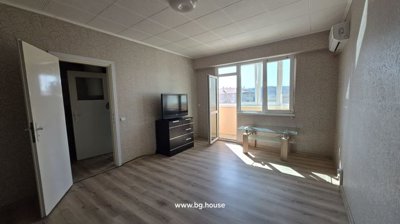 Bright living room featuring light wood flooring, patterned wallpaper, a TV on a black chest of drawers, and an open door leading to the balcony.