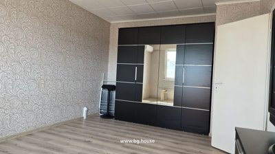 Living room featuring a large black wardrobe with a central mirror, a black stool, and a drying rack against patterned wallpaper.
