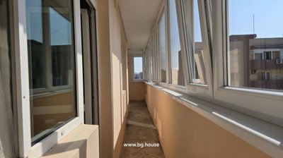 Long enclosed balcony corridor with multiple windows on one side and peach-colored walls, allowing natural light inside.