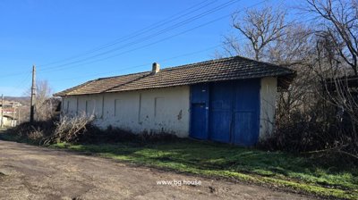 Side view of a white outbuilding featuring large blue wooden doors and a tiled roof next to a dirt road.