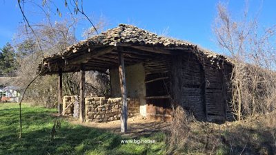 Barn structure featuring adobe walls and wooden posts standing in a grassy field.