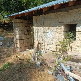 Close-up of stone wall exterior with small window and garden tools scattered nearby