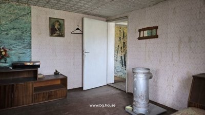 Interior room featuring patterned wallpaper, a white door leading to another room, wooden furniture, and a metal stove in the center.