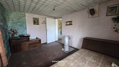 Interior room showing patterned wallpaper, a white door, wooden furniture, a metal stove, and a bed with patterned bedding.