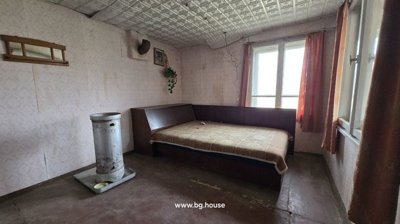 Interior room containing a bed with patterned bedding, a metal stove, window with curtains, and patterned wallpaper.