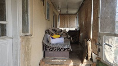 Enclosed veranda area containing stacked carpets, a sofa, and a door providing access to the interior of the house.
