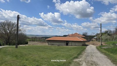 Grassy lawn area with stone building and dirt road leading away under blue sky with clouds