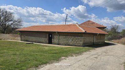 Exterior view of a single-storey building made of stone and brick with a red tiled roof and a black door.