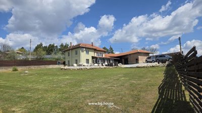 Two-storey house with green walls and red tiled roof, large grassy garden and gravel yard with stone borders