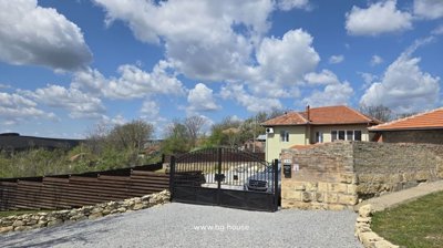 House viewed behind black metal gate with gravel driveway and stone wall on the right