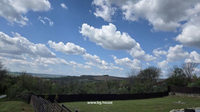 Grassy garden area bordered by wooden fence with hills and blue sky in the background
