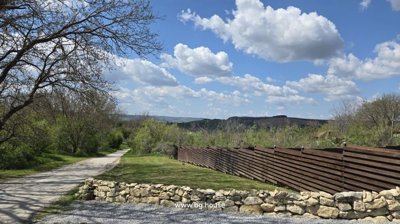 Grassy garden bordered by wooden fence with distant hills under partly cloudy sky