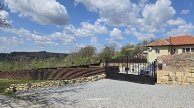 Gravel driveway bordered by stone and wooden fence leading to black metal gate