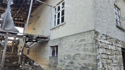View of the house corner showing stone and concrete foundation with an old wooden balcony frame