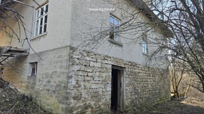 Side perspective of the house showing stone and concrete base with several windows and surrounding bare trees